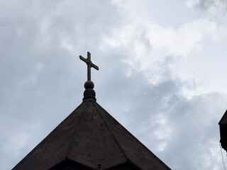 A cross is on top of a building. The building is surrounded by trees. The sky is blue