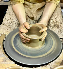 Hands of young potter working with clay and making vase or pot, jug or mug. Throwing pottery on wheel closeup.