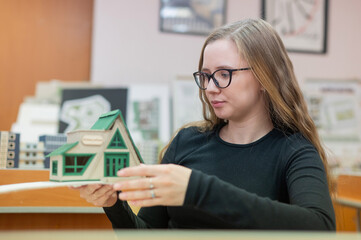 Caucasian young woman making a model of a building. Student of the construction university. 
