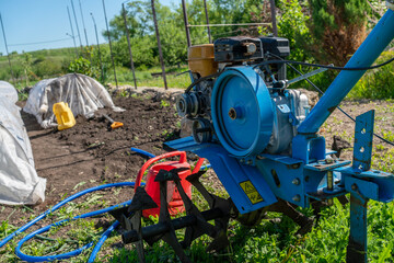 Red walk-behind tractor or tiller parked on grass in a rural garden. Agricultural machinery for soil cultivation.