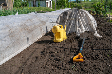 A watering can and a shovel are on the bed, ready for work. The shooting is taking place outdoors.