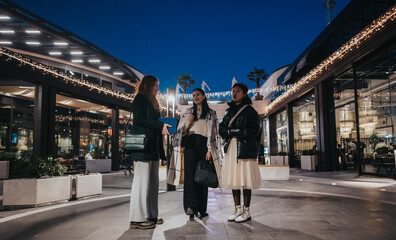 A group of young friends gathered outdoors at a decorated modern plaza during the evening. The...