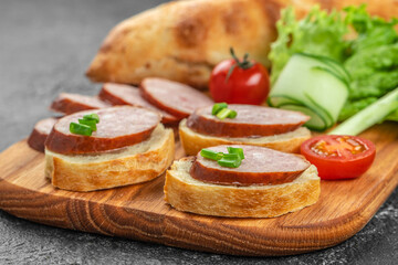 Slices of smoked sausage served on fresh bread with green onions and vegetables create a rustic and delicious appetizer on a wooden board