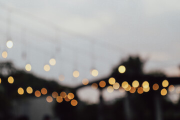 Defocused image of warm string lights hanging outdoors at dusk, creating a soft and dreamy bokeh effect against a gentle sky background