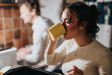 A young woman enjoys a warm drink in a cozy indoor setting, with a focus on relaxation and casual...