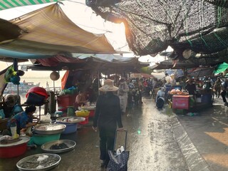 Vietnamese woman walking through a traditional market next to the river at sunrise. Morning light...