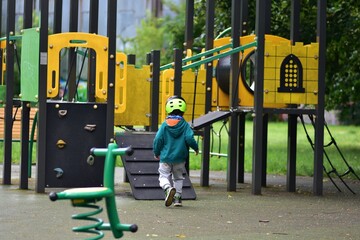 Young boy in helmet approaching colorful playground structure on a cloudy day. Child ready for...