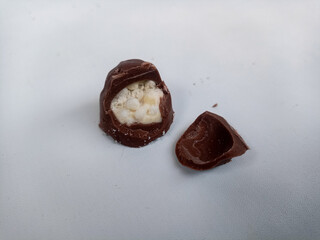 Close-up of chocolate-coated snacks with a crispy and creamy filling, displayed on a clean white background. One piece is bitten to reveal the textured inside, emphasizing indulgence and texture.