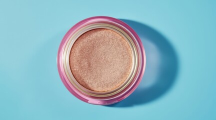 Close up overhead view of a shimmering rose gold highlighter compact on a teal background