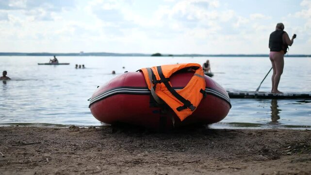 A rescue boat with a life jacket on the shore near the waves against the background of people floating in the water and a man on a SUP board. Rescuers' equipment.