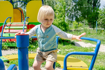 Cute funny blond little young toddler kid child boy sitting and riding on swing roundabout carrousel in playground park.Children physical,emotional development childhood daycare,kindergarten concept