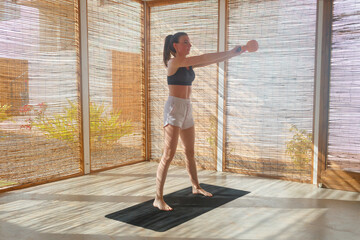 A woman performs an exercise routine with a weight, showcasing strength and focus in a spacious,...