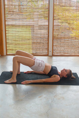 A woman performs the bridge pose on a yoga mat in a spacious studio with natural light and a...