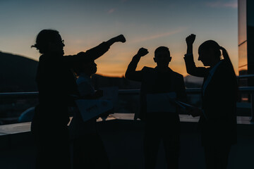 Four silhouetted business people celebrate a successful outcome outdoors at sunset, exuding team...