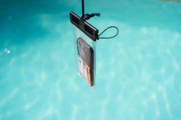 Waterproof case with money and a smartphone on the background of the pool on a sunny summer day