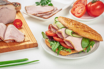 A fresh sandwich made with sliced ham, tomato, cucumber ribbons, and leafy greens is served on a...
