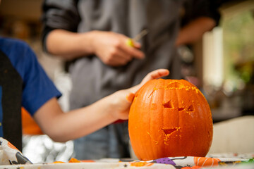 Young child shows off face of fresh pumpkin carved for Halloween. A parent stands in the background...