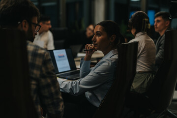 A group of business people working together in an office setting late at night, discussing...