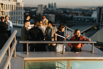 A group of business colleagues stand on a rooftop balcony, discussing ideas and solutions. The...