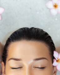 Close-Up Of Womans Face With Flowers And Closed Eyes In Spa Water