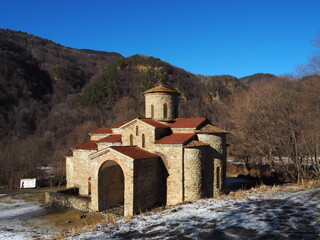 Historic stone church nestled in a mountainous landscape during winter with clear blue skies