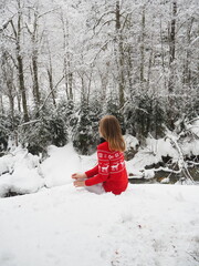 Person in a red sweater sitting quietly by a snowy stream surrounded by frosty trees during winter