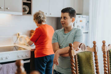 A young boy stands near a kitchen counter, seemingly in conversation, as an elderly woman busily...