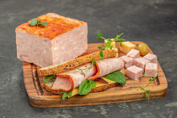 A hearty sandwich with rolled ham slices, cheese, and greens is served on a wooden board next to a...