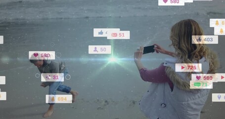 woman filming man dancing on beach with animated social icons increasing engagement - Powered by Adobe