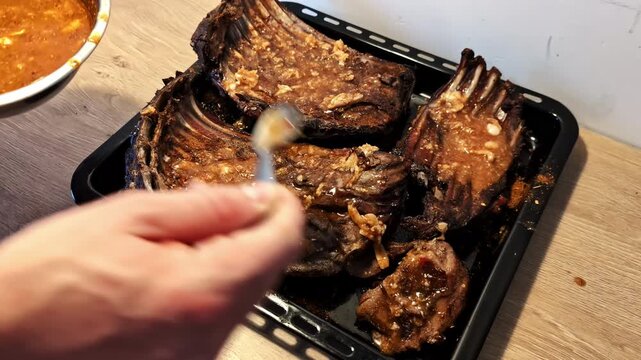 Roasted ribs on a tray being basted with a chunky, flavorful sauce