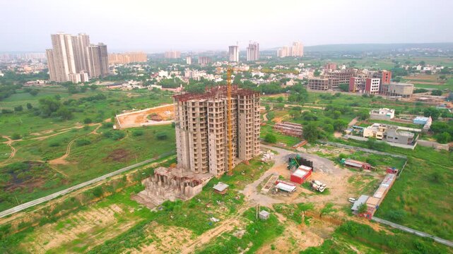Aerial drone shot orbiting under construction building with trucks and mixers parked in the front and delhi cityscape in distance showing rapid development of housing projects