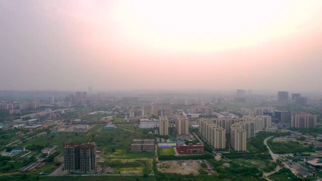 Aerial drone shot flying forward over sunset malls with skyscraper multistory buildings and green fields