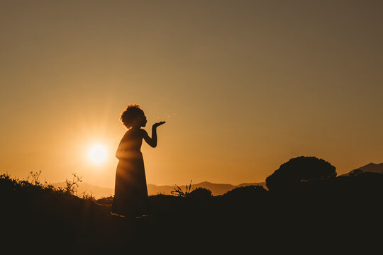 Silhouette of black little girl blowing dandelions at sunset beach