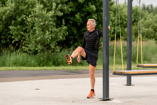 Senior man exercising his leg on a swing set in a city park.
