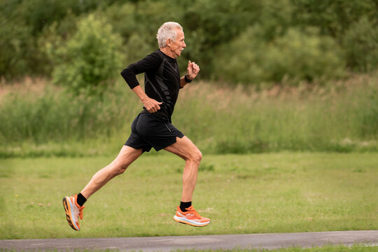 An elderly man running on a paved path in a green park.