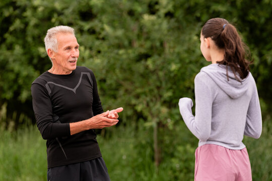elderly trainer gives instructions to a young athlete in the park.