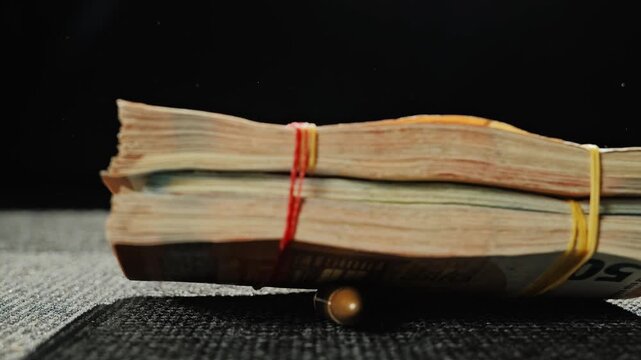 9mm round toppled by falling rubber-banded euro bills in moody dark setting