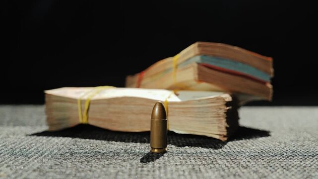 Close up of bullet and rubber-banded banknotes on fabric surface with hard light
