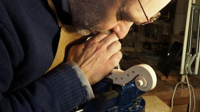 Skilled violin maker carves a new scroll with precision, following a traditional Cremonese school model, using hand tools in a dedicated workshop environment.