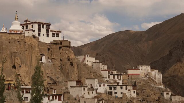Gompa nestled on cliff with dramatic mountainous landscape, Timelapse with moving shadow and light from dynamic clouds.