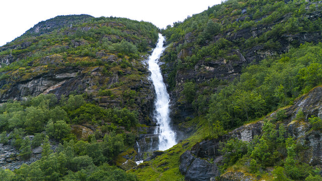 Aerial view of Turlifossen waterfall cascading down a rugged mountain face, where white water contrasts with the dark rocks and verdant greenery, Aurland, Vestland, Norway.