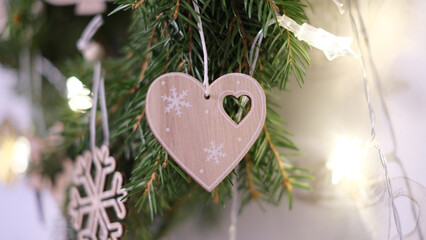Elegant close-up of a wooden heart-shaped Christmas ornament adorned with delicate snowflake patterns and a heart cut-out, hanging gracefully on a festive fir branch