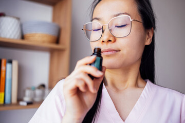 A young Asian woman in casual clothing smelling an essential oil. An attractive Korean woman...