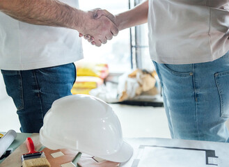 A construction helmet, male and female hands joined in a handshake. A man and a woman shake hands,...