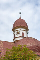 Wooden church with a white tower with clock With Roman numerals and gold hands and red domes and...