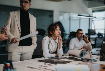 A diverse group of business people brainstorms ideas around a conference table in a modern, busy...