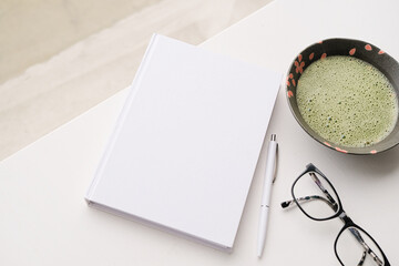 blank book mockup on white coffee table with green matcha tea near window