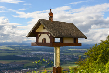 Bird feeder house in the form of a small church The house is set on poles. A large city is visible in the background.