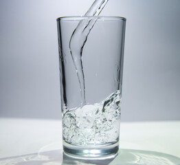 A stream of water flows into a transparent glass The water swirls at the bottom of the glass.