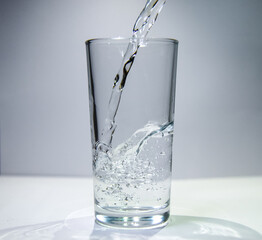 A stream of water flows into a transparent glass The water swirls at the bottom of the glass.